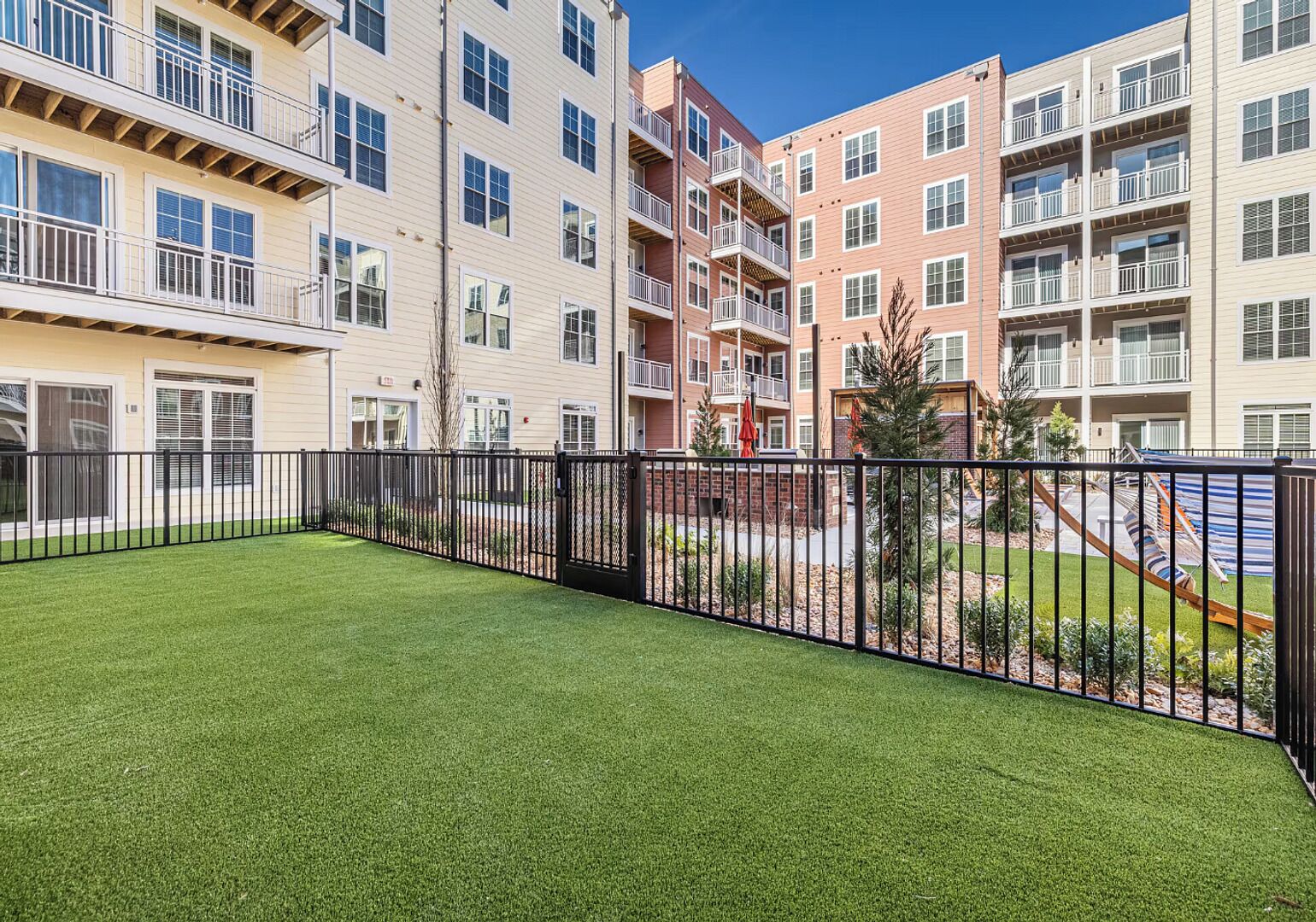 A multi-story residential building with balconies, a fenced yard, and a well-maintained lawn.