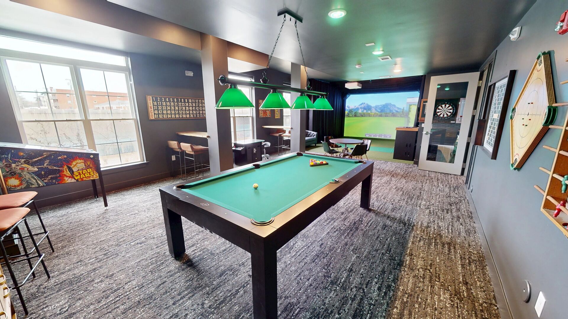 Une table de billard recouverte d’un feutre vert, une œuvre d’art sur le thème de Star Wars et un jeu de fléchettes.