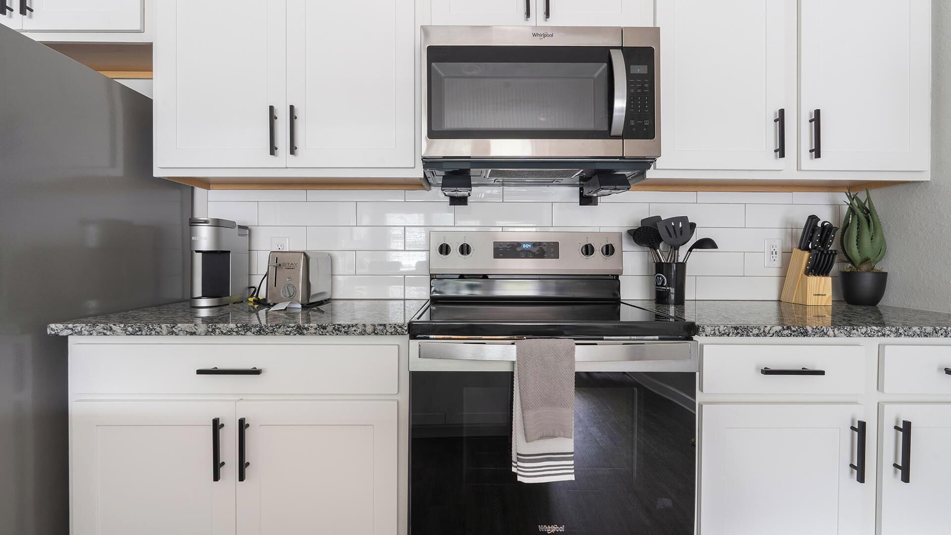 A modern kitchen with white cabinets, a built-in microwave, a coffee maker, a toaster, and a stove.