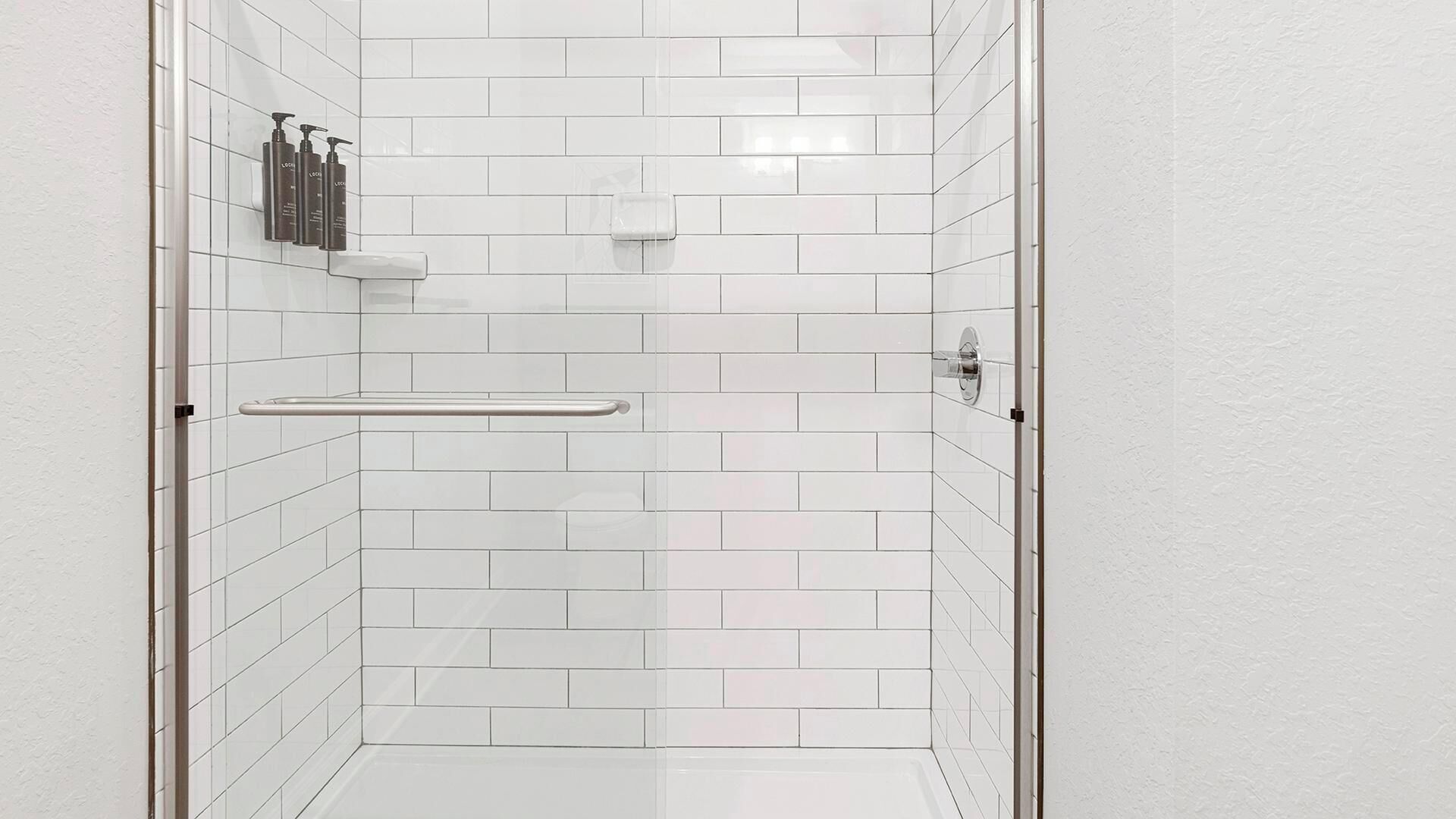 Una ducha con paredes de azulejos blancos y puerta de vidrio.