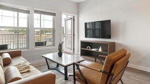 A living room with a sofa, coffee table, TV, and a bookshelf. - Landing | Stylish 1BD, Pool, Gym (Palm Bay)