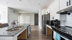 Uma cozinha moderna com bancada de granito, eletrodomésticos de aço inoxidável e piso de madeira.