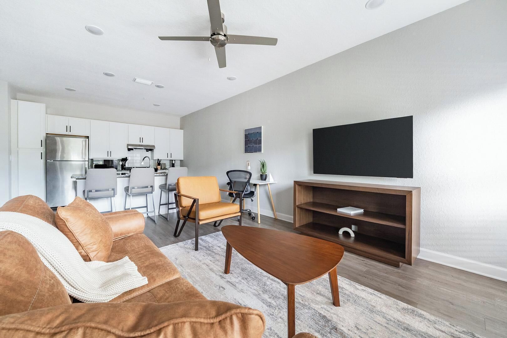 Un salon moderne avec un canapé, une table basse, un téléviseur et une cuisine en arrière-plan.