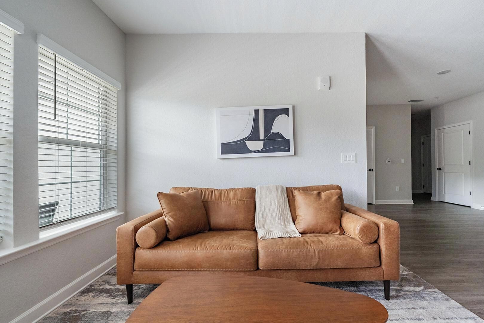 Un salon avec un canapé en cuir couleur fauve, un plaid blanc et un tableau abstrait moderne accroché au mur.