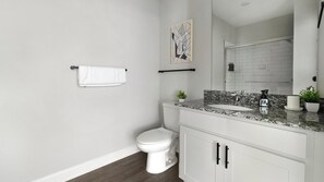 Casa de banho com sanita, lavatório, espelho, porta-toalhas e uma pequena planta em vaso.