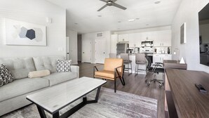 Een moderne woonkamer met een bank, salontafel en een eethoek met stoelen, en een keuken op de achtergrond.