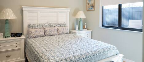 A bedroom with a bed, nightstands, a window, and artwork on the walls.