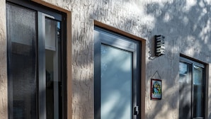 Um edifício com fachada texturizada, uma porta com puxador e um tapete de boas-vindas.