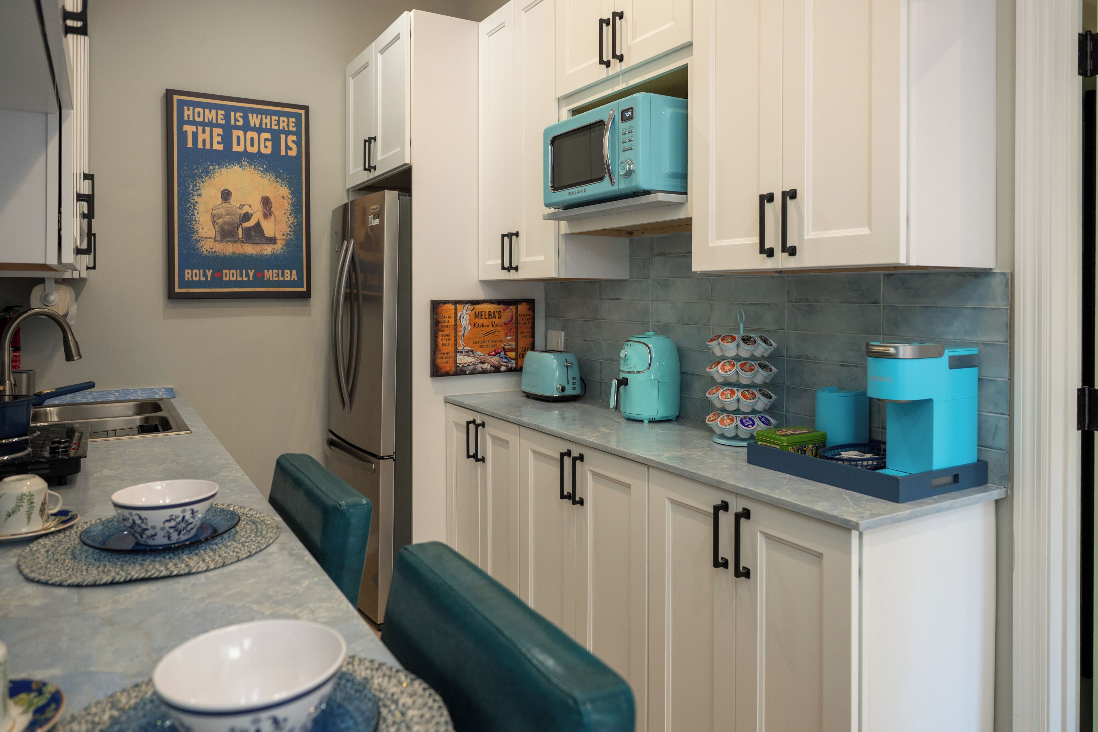 Una cocina con armarios blancos, microondas azul, cafetera y un bol sobre la encimera.