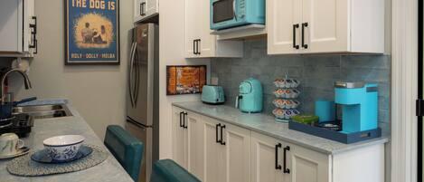 Una cocina con armarios blancos, microondas azul, cafetera y un bol sobre la encimera.