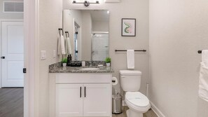 Une salle de bain avec des toilettes blanches, un lavabo doté d’un plan de travail en granit, un miroir et un porte-serviettes.