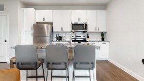 A modern kitchen with white cabinets, stainless steel appliances, and a granite countertop. - Landing | Amazing 1BD, Gym, Pool (Palm Bay)