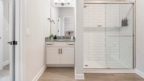 A bathroom with a shower, a sink with a mirror, and cabinets. - Landing | Spectacular 2BD, Pool, Gym (Palm Bay)