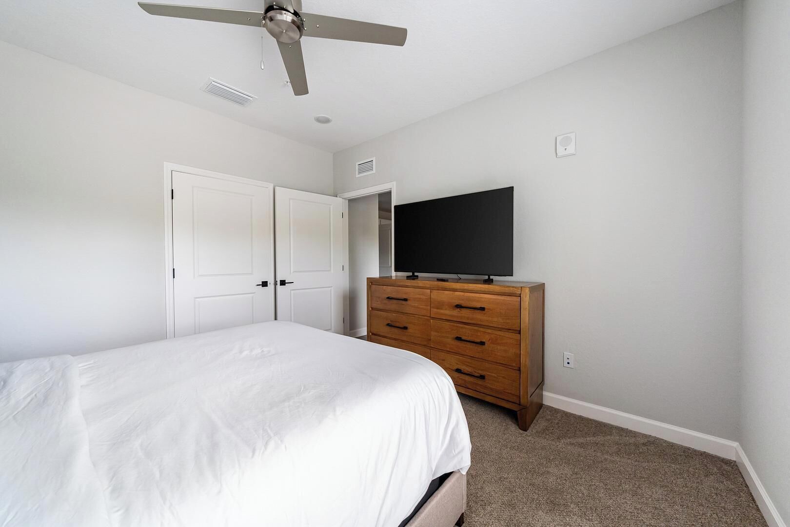 Ein Schlafzimmer mit Bett, Kommode, Fernseher und Deckenventilator.