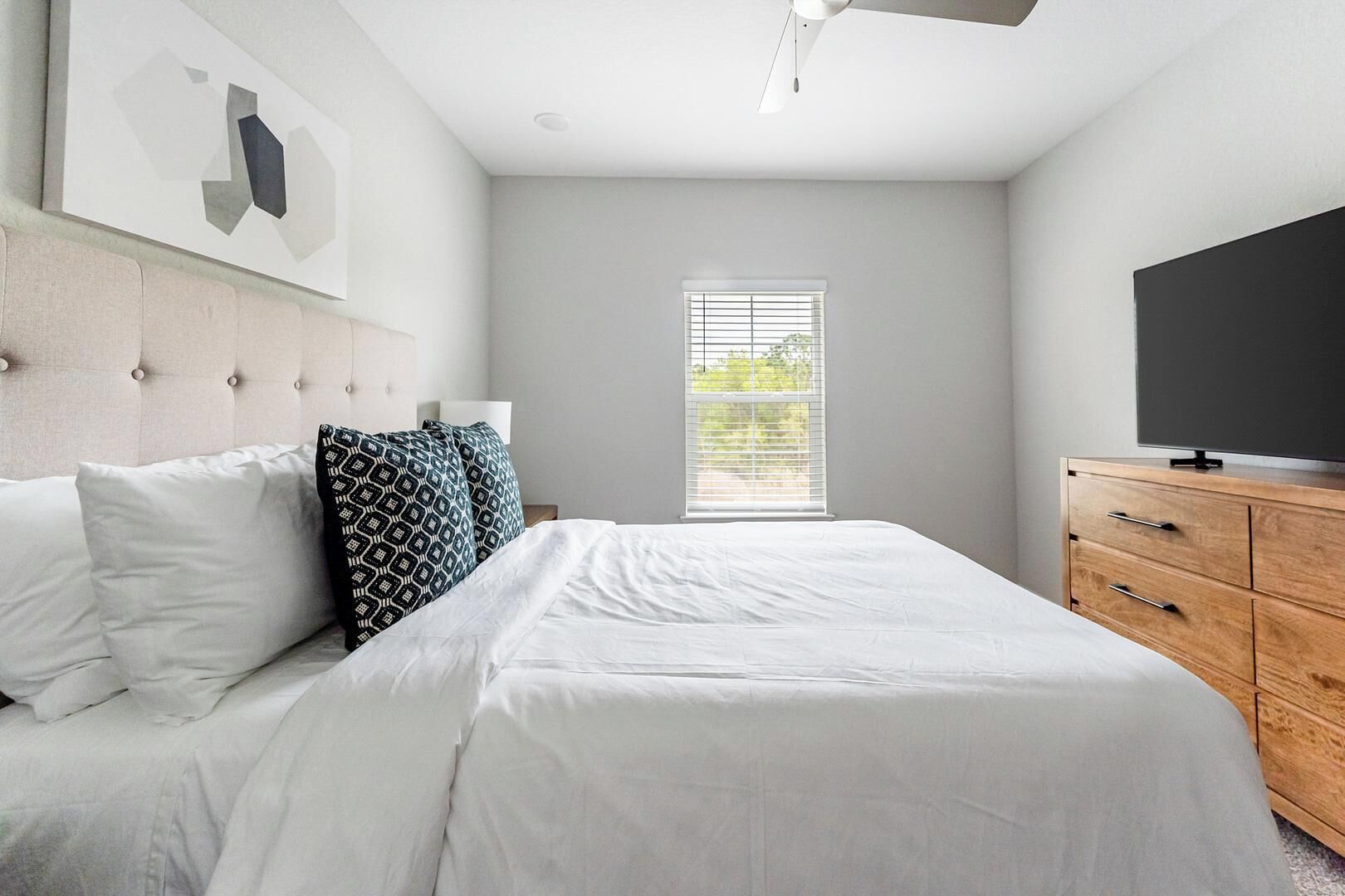 Un dormitorio con cama, cómoda de madera, televisor y ventana con persianas.