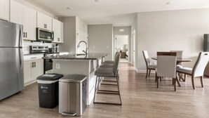 A modern kitchen with stainless steel appliances, a central island, and a dining area with chairs. - Landing | Stylish 2BD, Gym, Pool (Palm Bay)