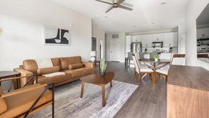 A modern living room with a sofa, coffee table, and dining area. - Landing | Stylish 2BD, Gym, Pool (Palm Bay)