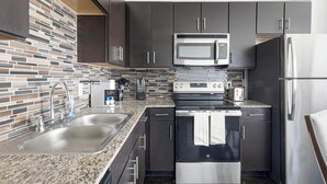 Eine moderne Küche mit Granit Arbeitsplatten, Edelstahlgeräten und dunklen Schränken.