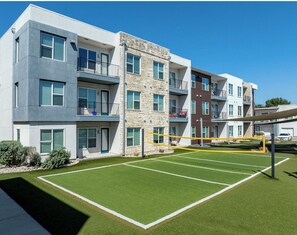 Um edifício residencial com vários andares, varandas, quadra de tênis e área de estacionamento.