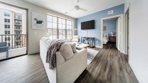 A modern living room with a sofa, a flat-screen TV, and a balcony. - Landing | Modern 1BD, Gym, Clubhouse (Cleveland)