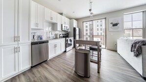 A modern kitchen with white cabinets, stainless steel appliances, and a wooden dining table. - Landing | Modern 1BD, Gym, Clubhouse (Cleveland)
