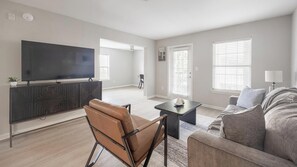 Un salon moderne avec un téléviseur à écran plat, un fauteuil en cuir, un canapé et une table à manger.