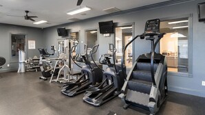 Ein Fitnessraum mit Laufbändern, Crosstrainern und einem Deckenventilator.