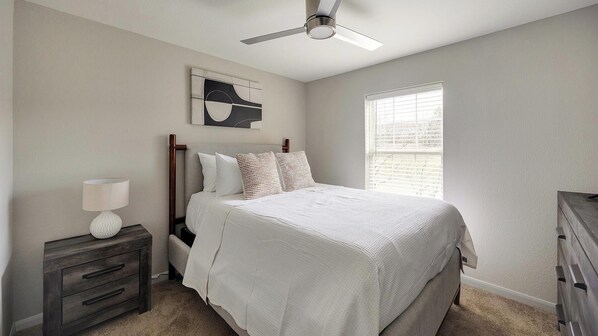 A bedroom with a bed, nightstand, lamp, ceiling fan, artwork, and a window. - Landing | Modern 2BD, Gym, Clubhouse (Charlottesville)