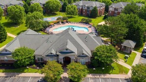 Zona residencial con piscina rodeada de sillones de descanso, cancha de tenis y un pequeño edificio.