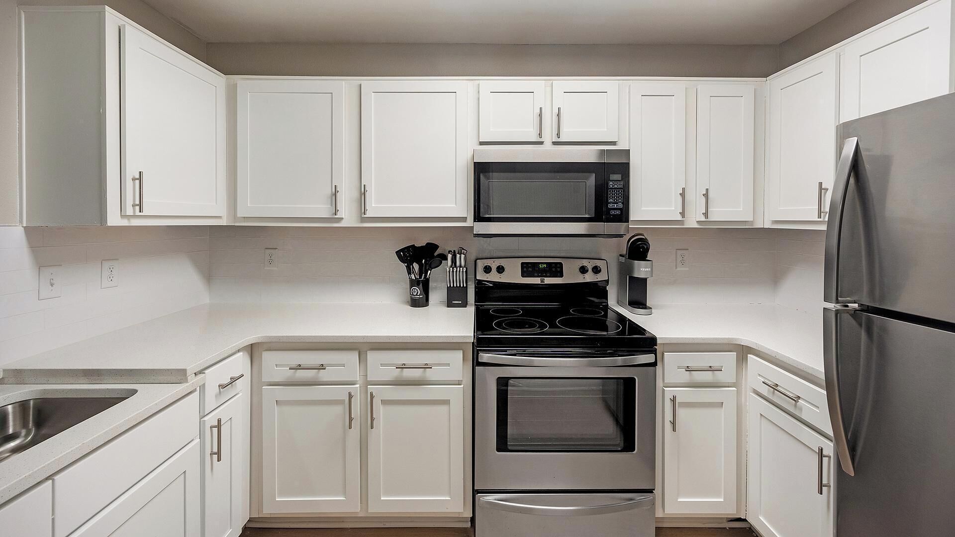 A modern kitchen with white cabinets, stainless steel appliances, and a built-in oven.