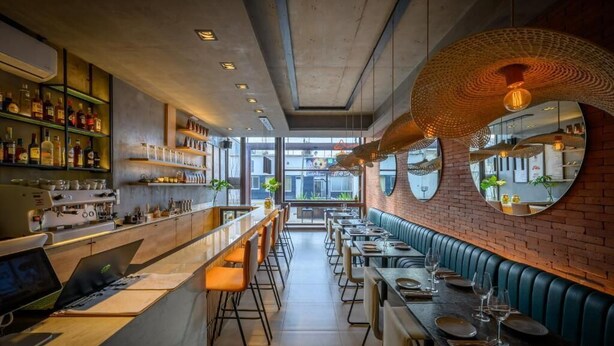 A restaurant with a bar area, long communal tables, and a brick wall with circular mirrors. - CB Mona Suites (Villa Mercedes)