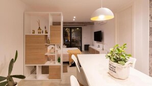 A modern living room with a white sofa, a dining table with a potted plant, and a TV mounted on the wall. - CB Mona Suites (Villa Mercedes)