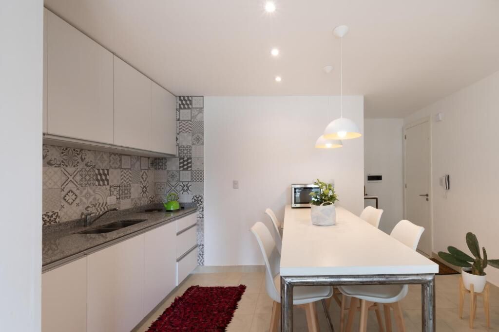 A modern kitchen with patterned backsplash, white cabinets, a central island, and a dining area with a white table and chairs.