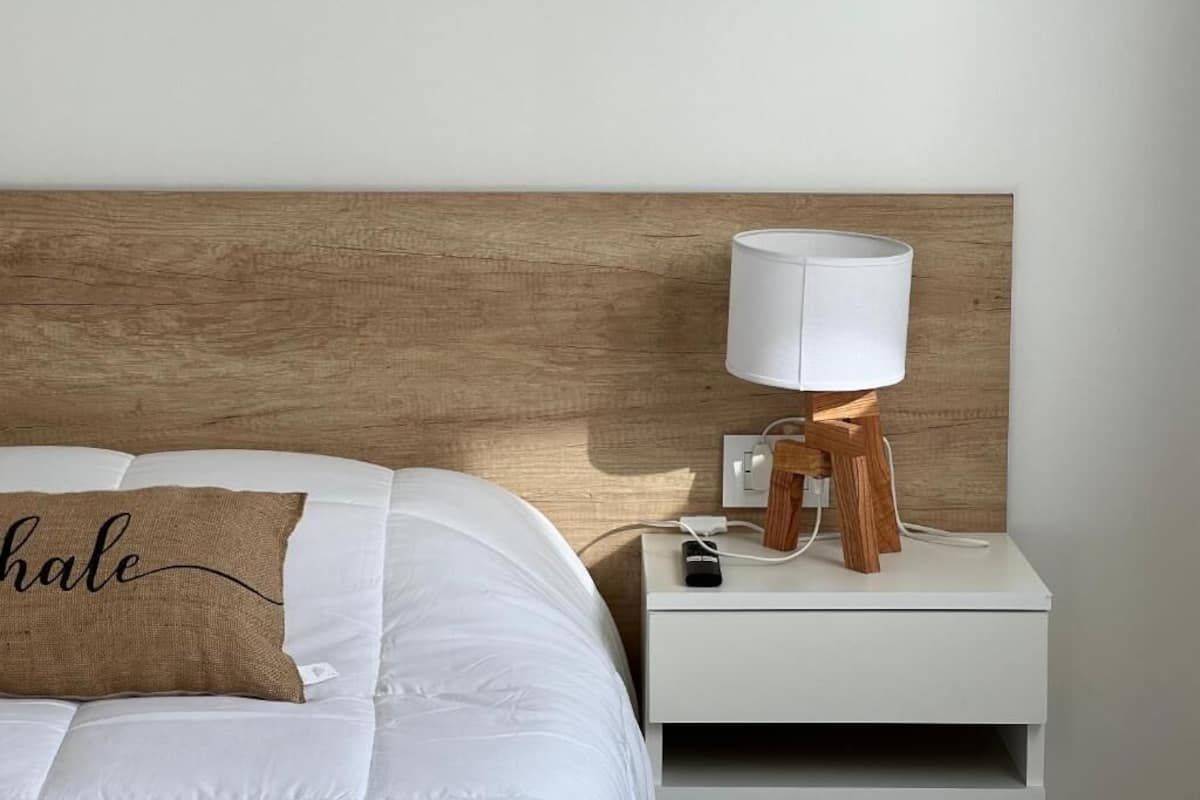 A neatly made bed with a pillow, a bedside table with a lamp, and a wooden headboard.