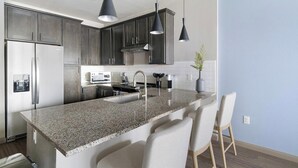 Una cocina moderna con encimeras de granito, electrodomésticos de acero inoxidable y barra para sentarse.