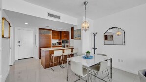 A modern kitchen with a bar area, white dining table, and chairs, and a chandelier. - LUXORA 2BR 1 BA 16TH FLOOR W -FREE SPA (Miami)