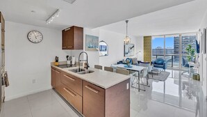 A modern kitchen with a central island, a dining area with a table and chairs, and a large balcony with a view of the city. - LUXORA 2BR 1 BA 16TH FLOOR W -FREE SPA (Miami)