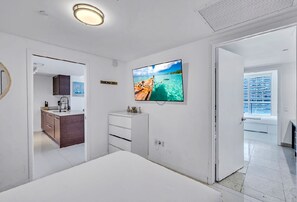 Ein modernes Hotelzimmer mit Bett, Wandfernseher, kleinem Schminktisch und Meerblick durch das Fenster.