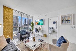 Ein modernes Wohnzimmer mit großem Fenster, einem Flachbildfernseher und Blick auf eine Stadtansicht.