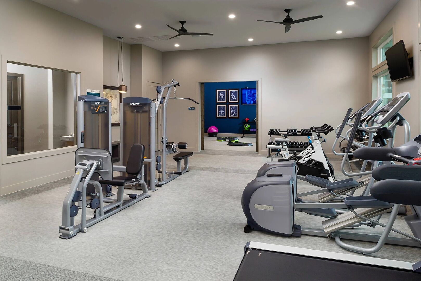 Une salle de sport équipée de divers appareils d’exercice, notamment des tapis de course et des appareils de musculation, ainsi qu’un grand écran de télévision diffusant des programmes sur le fitness.