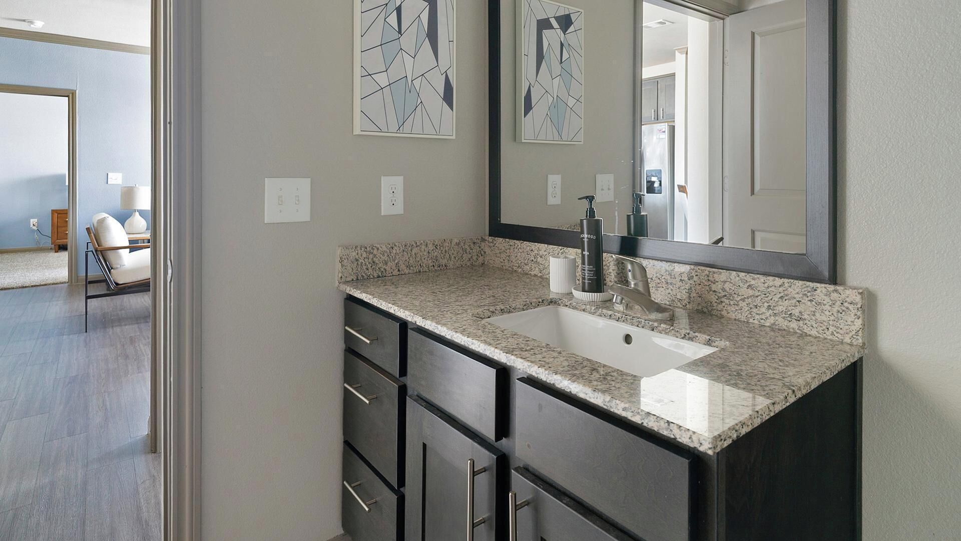 A bathroom with a granite countertop, a sink, a mirror, and a dark cabinet with drawers.