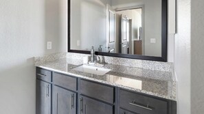 A bathroom with a granite countertop, a white sink, a mirror, and dark cabinetry. - Landing | Modern 2BD in Eastpoint (Baytown)