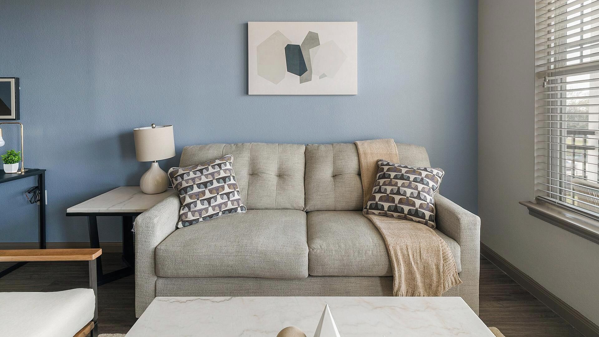 A living room with a sofa, two pillows, a lamp, a table, and a painting on the wall.