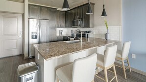 Eine moderne Küche mit Granit Arbeitsplatten, Edelstahlgeräten und Barhocker.
