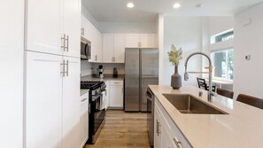 Una cocina moderna con armarios blancos, electrodomésticos de acero inoxidable, horno empotrado e isla grande con pileta.
