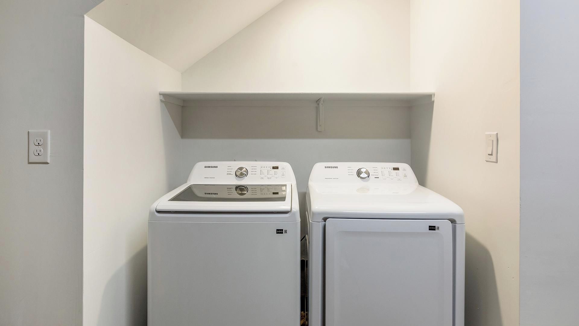 Une buanderie équipée de deux machines à laver Samsung blanches, avec une étagère placée au-dessus.
