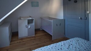 Ein Schlafzimmer mit schrägen Wänden, einem Babybett, einem kleinen Schrank und einer Tür.