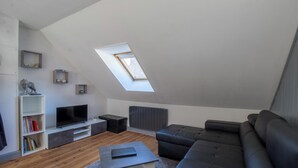 Ein Loft-Wohnzimmer mit schrägem Dach, Dachfenster, einem Flachbildfernseher, einer Eckcouch und eingebauten Regalen.