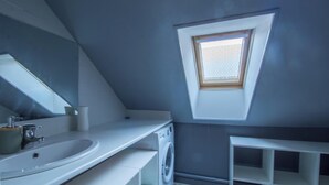 Ein modernes Badezimmer mit Dachfenster, großem Spiegel, Waschbecken, Waschmaschine und weißem Waschtisch.