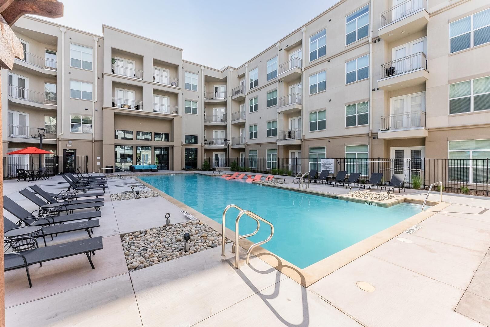 A multi-story hotel with a swimming pool, lounge chairs, and a small outdoor seating area.